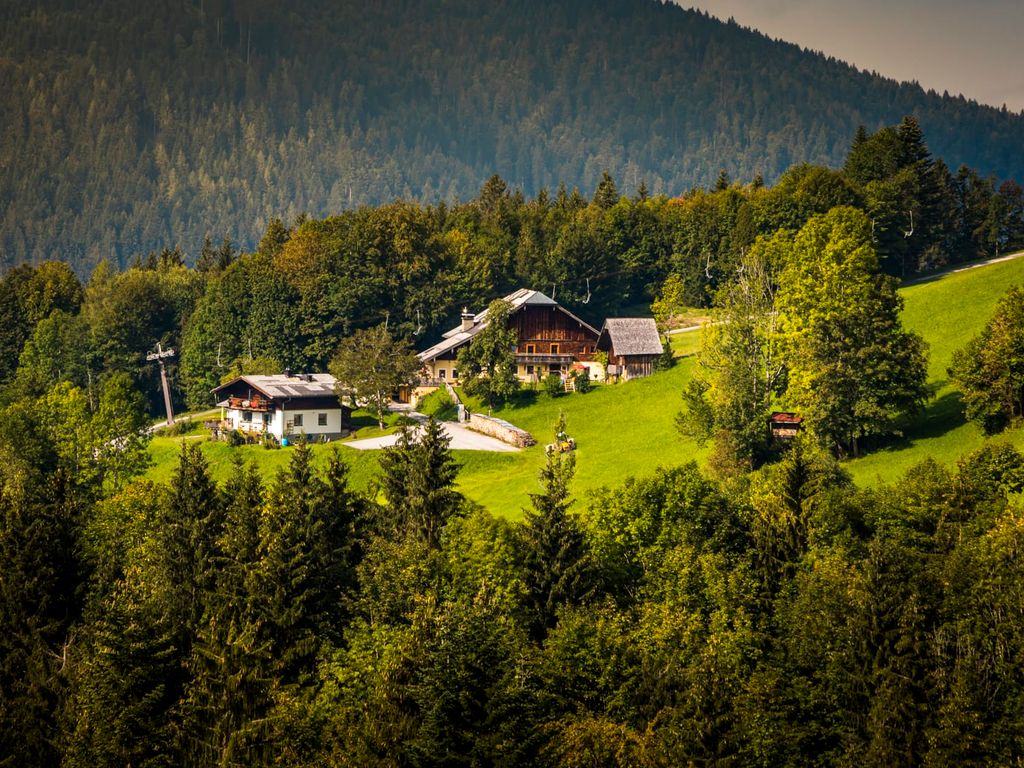 Der Bauernhof auf einem grünen Hügel, umgeben von Wäldern und Bergen.