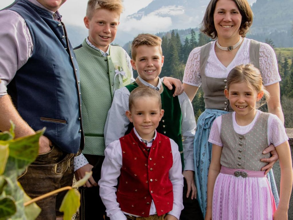 Die Gastgeberfamilie des Bauernhofs in traditioneller Kleidung vor alpiner Kulisse.