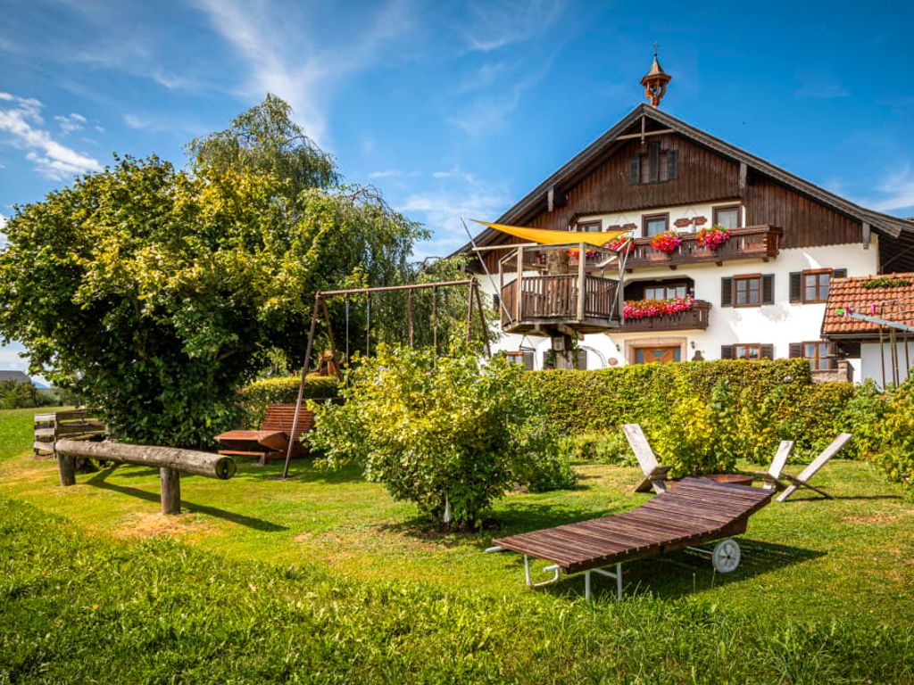 Der einladende Garten des Bauernhofs mit einer großen Liegewiese, Sonnenliegen und einem Kinderspielplatz vor dem traditionellen Haupthaus.