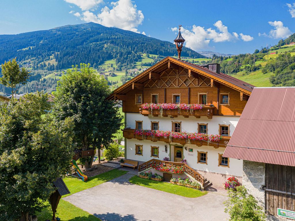 Der Bauernhof mit blumengeschmückten Balkonen und traditioneller Architektur vor der Kulisse der Alpen, inklusive Kinderspielplatz.
