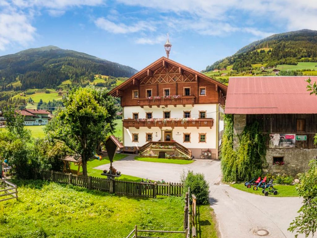 Der einladende Bauernhof im traditionellen Alpendesign, umgeben von einer weitläufigen grünen Wiese und den sanften Berghängen.