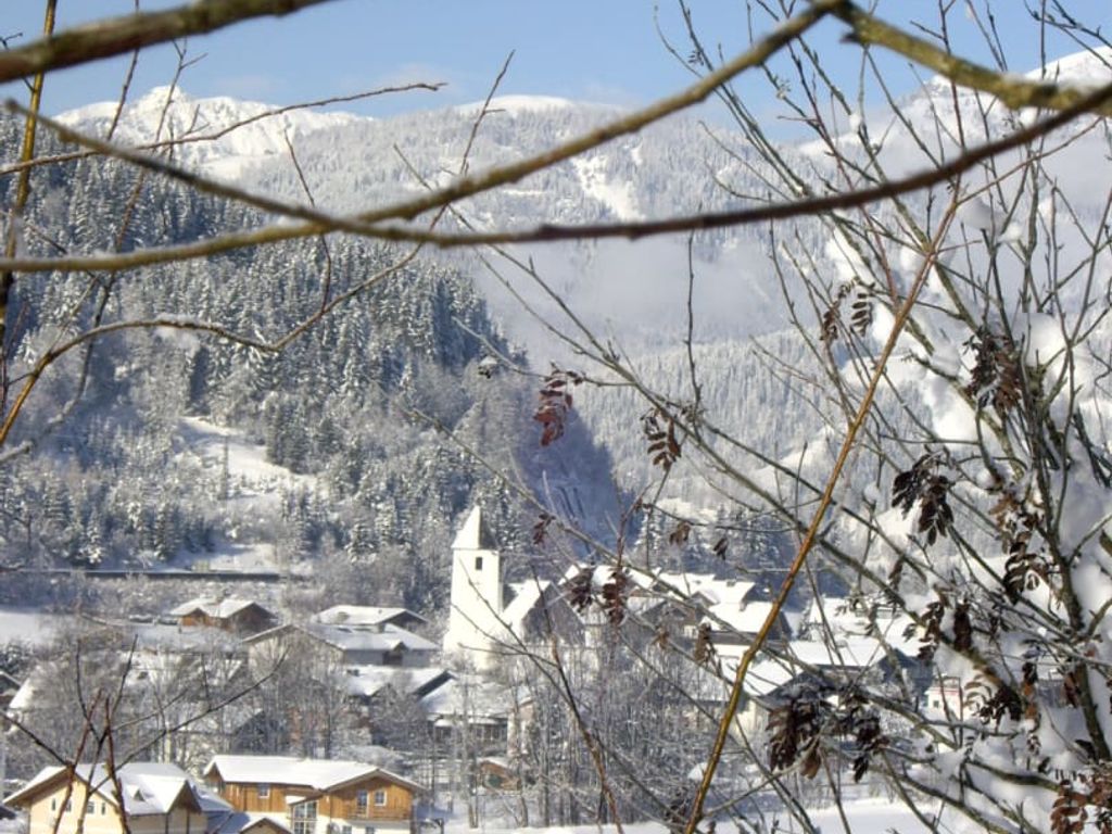 Blick auf ein verschneites Dorf mit Kirche und Berglandschaft vom Bauernhof aus.