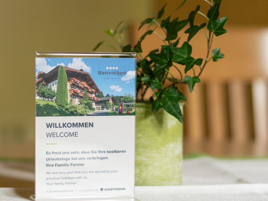 Willkommensschild für den Bauernhof auf einem Tisch, daneben eine Zimmerpflanze.