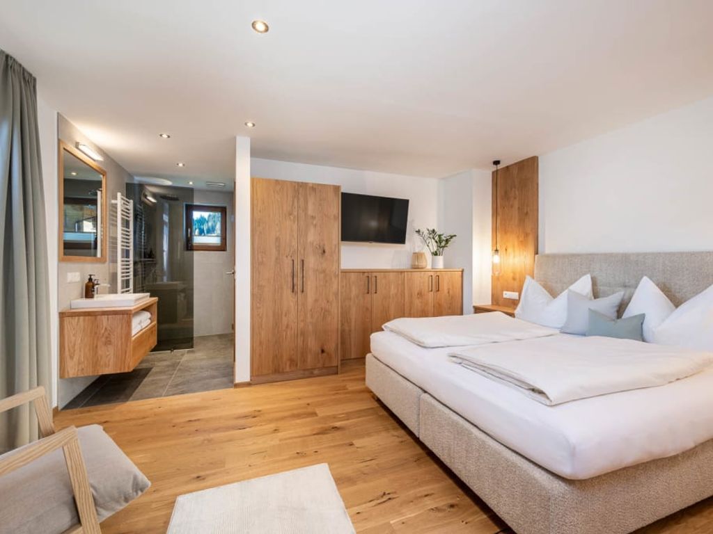 Schlafzimmer in der Ferienwohnung mit Doppelbett, Holzmöbeln, Fernseher und offenem Badbereich mit Dusche.