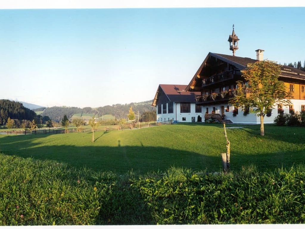 Der Bauernhof mit Glockenturm, umgeben von grünen Wiesen und bewaldeten Hügeln, inklusive Schaukel auf dem Gelände.