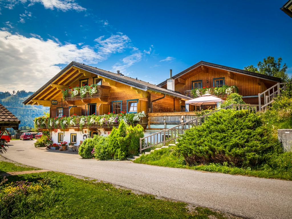 Der Bauernhof von außen mit traditioneller Holzfassade, blumengeschmückten Balkonen und Zufahrtsweg vor der Salzburger Bergwelt.