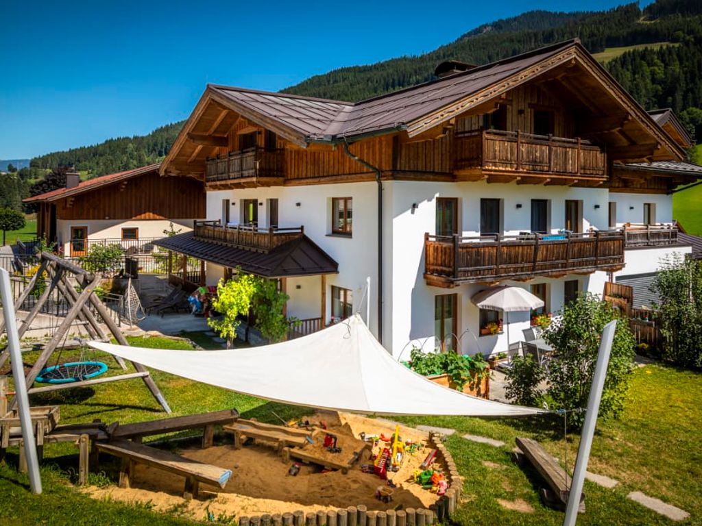 Der sonnige Außenbereich des Bauernhofs mit einem einladenden Kinderspielplatz samt Sandkiste und Schaukel.