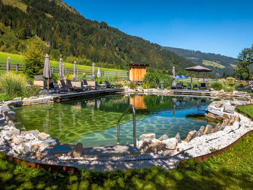Der einladende Naturbadeteich des Bauernhofs mit einer sonnigen Liegewiese, gemütlichen Liegestühlen und herrlichem Bergblick.