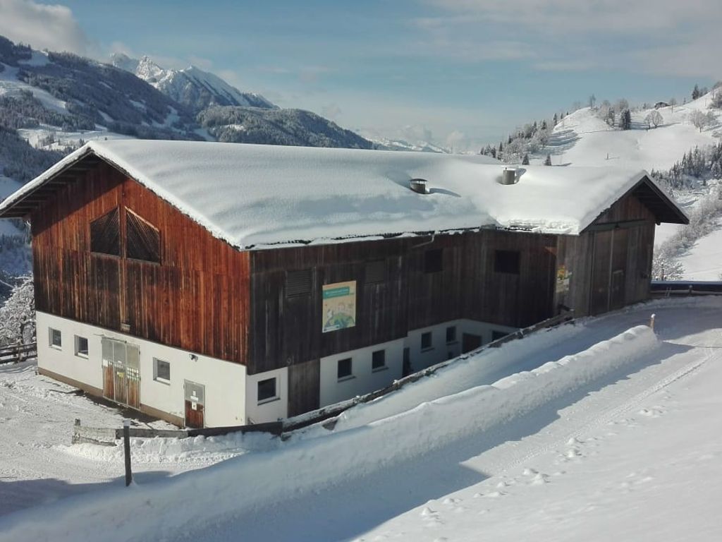 Das Hauptgebäude des Bio Bauernhofs im Winter, mit verschneitem Dach und Blick auf die umliegende Berglandschaft.