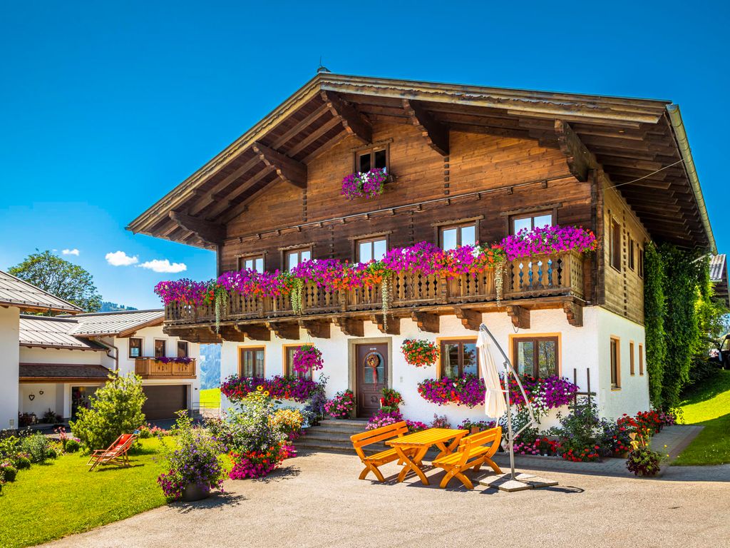 Der Bauernhof mit seiner traditionellen Holz- und Putzfassade, blumengeschmückten Balkonen und einem Sitzbereich im Freien.