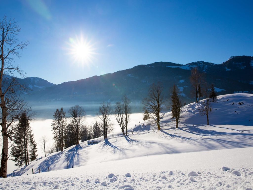 Winterliche Berglandschaft mit verschneiten Hängen, strahlender Sonne und Nebel im Tal.