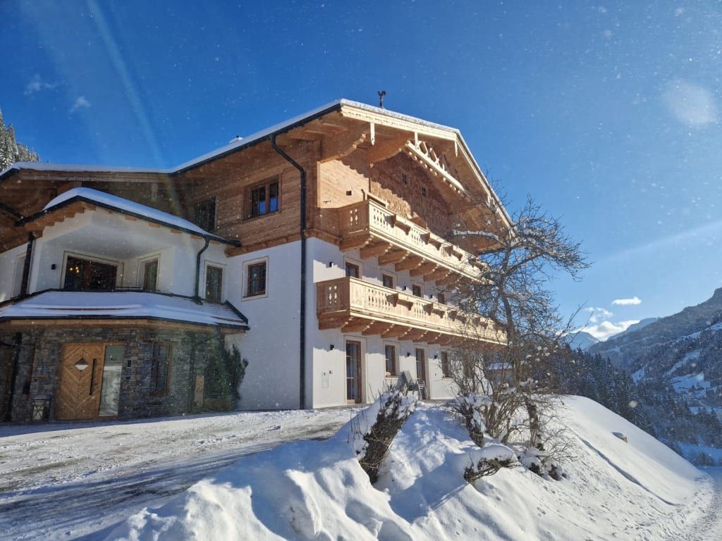 Außenansicht des Bauernhofs im Winter, mit traditioneller Architektur, Holzbalkonen und schneebedeckter Landschaft.