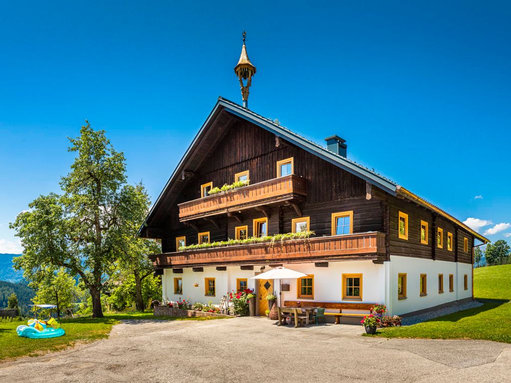 Außenansicht des Bio-Bauernhofs Steinerhof mit traditioneller Holzfassade, Balkonen, einem Sitzbereich im Freien und umgebenden Wiesen mit Bergblick.