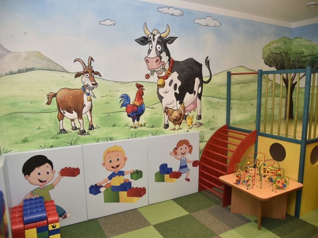 Der Kinderspielbereich im Bauernhof mit Wandgemälde von Bauernhoftieren, einer kleinen Spielstruktur und einem Spieltisch mit Motorikschleife.