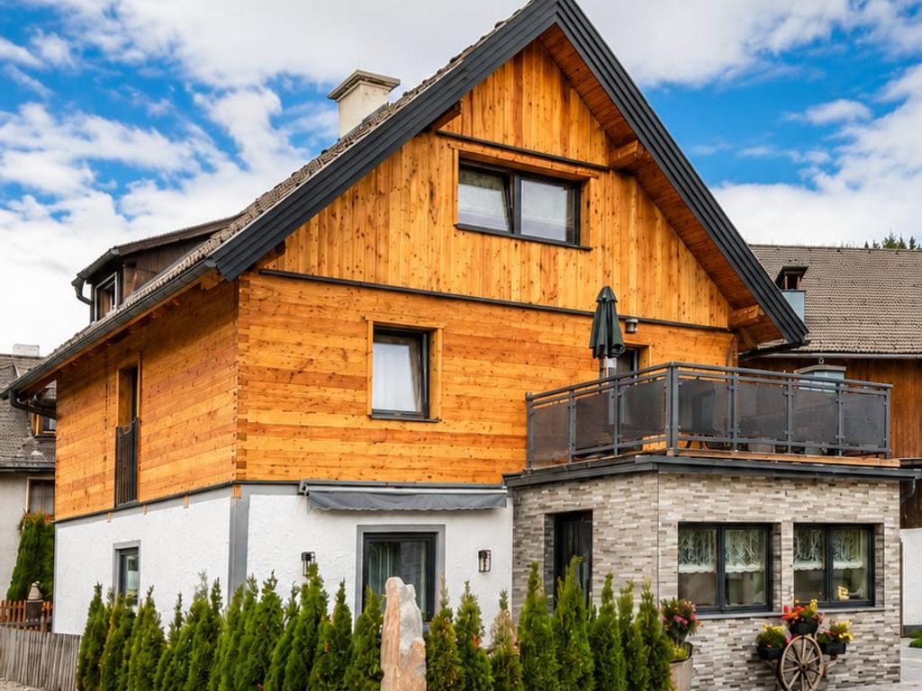 Die charmante Außenansicht des Bauernhofs mit rustikaler Holzfassade, Balkon und gepflegten Hecken.