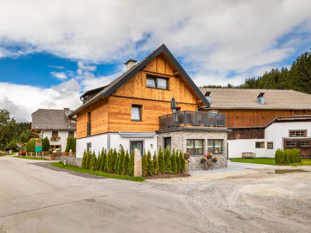 Außenansicht des Bauernhofs mit Holzfassade, Balkon und Schotterparkplatz.