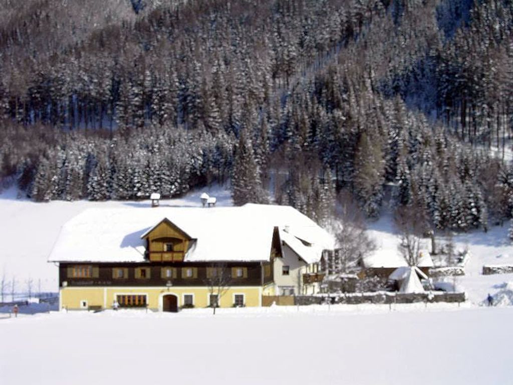Außenansicht des Bauernhofs in einer verschneiten Winterlandschaft mit angrenzendem Waldhang.