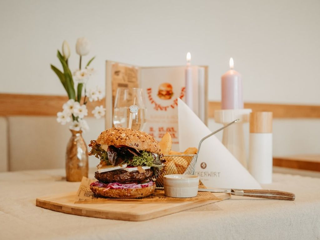 Burger mit Pommes und Dip, serviert auf einem Holzteller im Restaurantbereich des Bauernhofs.