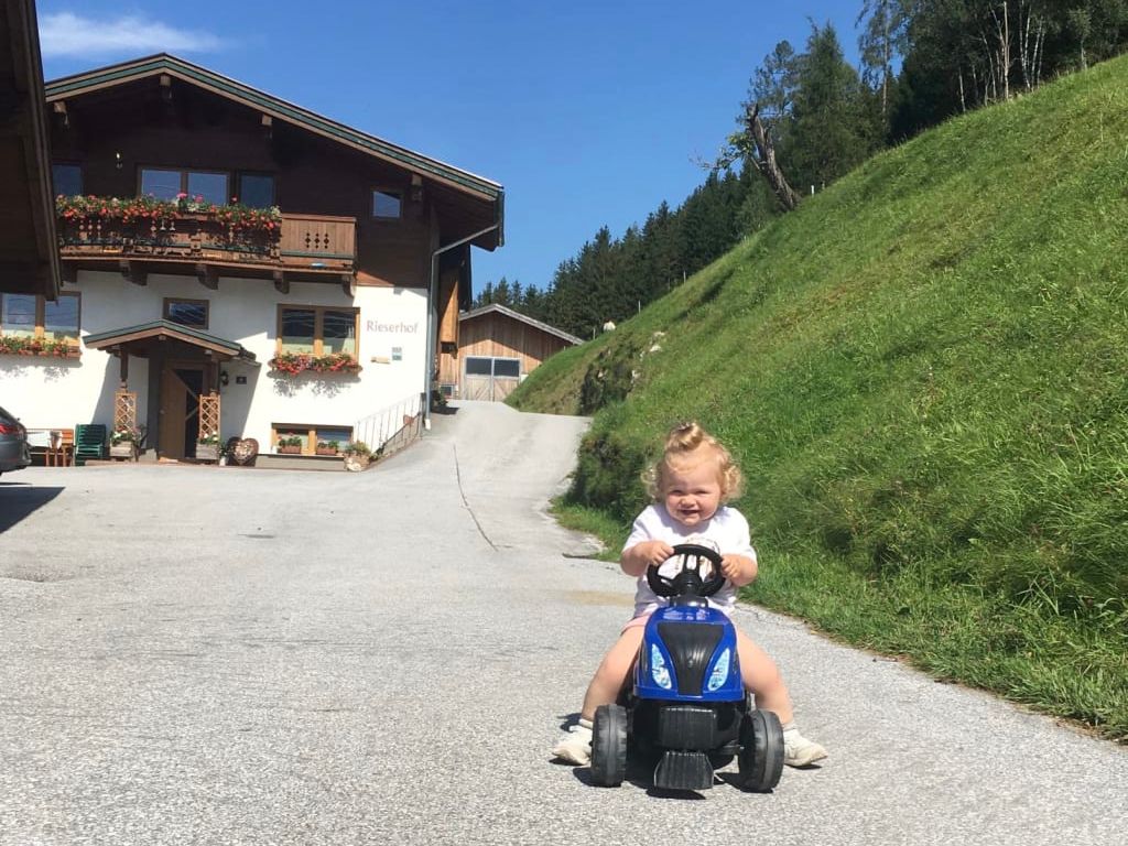 Ein Kind fährt auf einem Spielzeugtraktor vor dem Bauernhof, der kinderfreundliche Einrichtungen bietet.