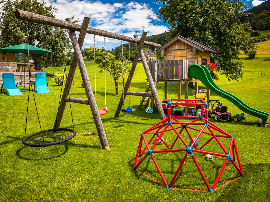 Der Kinderspielplatz auf dem Bauernhof bietet ein Schaukelgestell, eine Kletterkuppel und ein Spielhaus mit Rutsche.