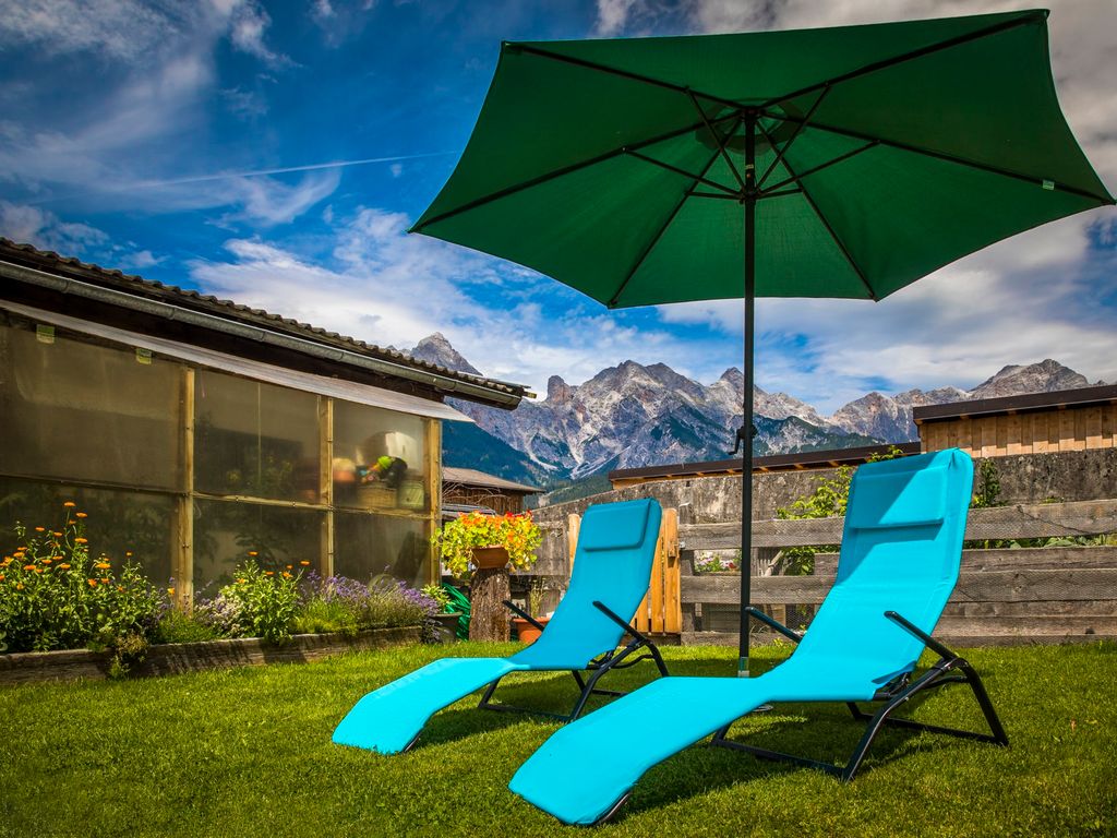Der Garten des Bauernhofs mit Sonnenliegen, Sonnenschirm und Bergblick.