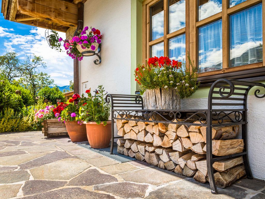 Der gepflasterte Außenbereich des Bauernhofs mit Blumendekoration und einem Holzstapel an der Hauswand.