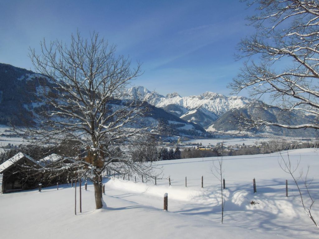 Blick vom Bauernhof auf die verschneite Winterlandschaft mit Bergen und einem Dorf.