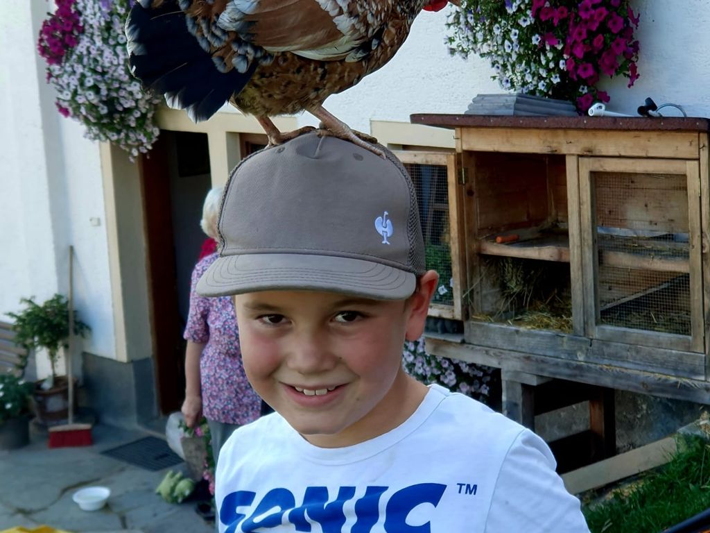 Kinder erleben auf dem Bauernhof Tiere, wie hier ein Huhn, das auf der Mütze eines Kindes sitzt.