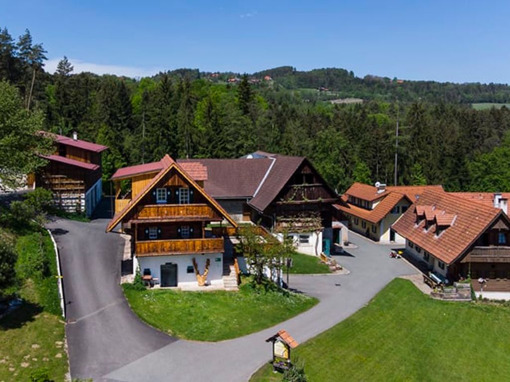 Der Bauernhof mit mehreren traditionellen Gebäuden, Zufahrtswegen und umgeben von Wald und grünen Wiesen.