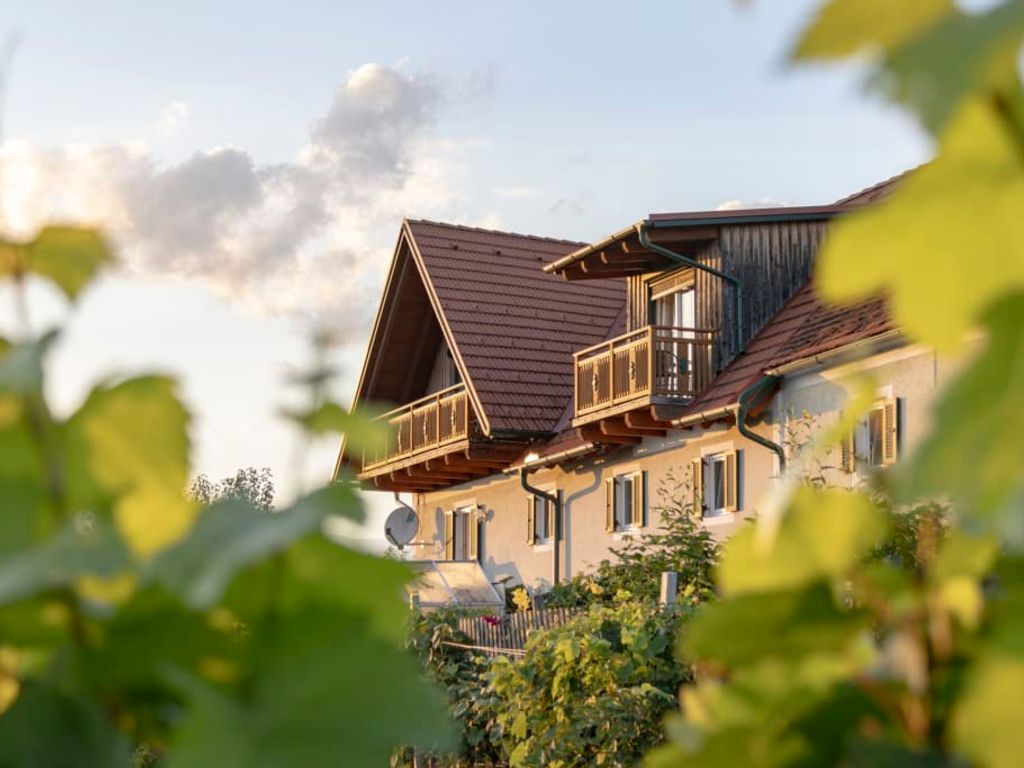 Der einladende Bauernhof mit seinen traditionellen Holzgbeln und Balkonen, sanft eingerahmt von grünen Weinreben.