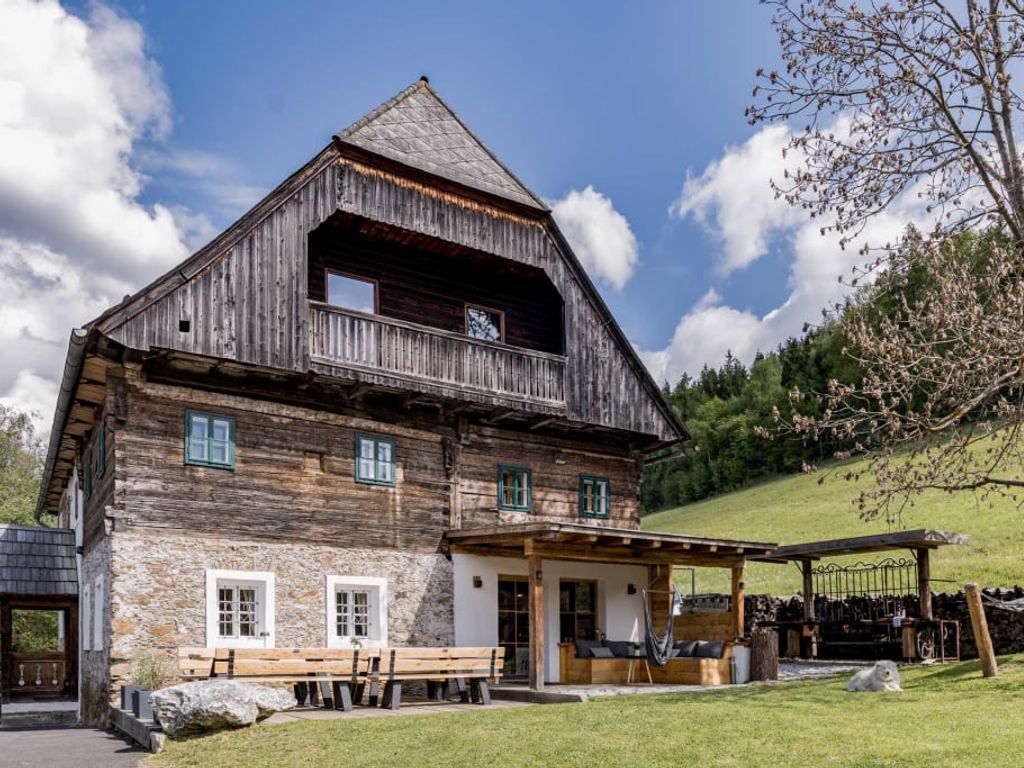Die Außenseite des Bauernhofs mit traditioneller Holz- und Steinfassade, einem Balkon und einer überdachten Terrasse mit Sitzgelegenheiten im Garten.