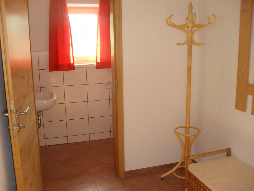 Eingangsbereich des Bauernhofs mit Garderobe, Sitzbank und Blick in ein Badezimmer mit Waschbecken und Fliesen.