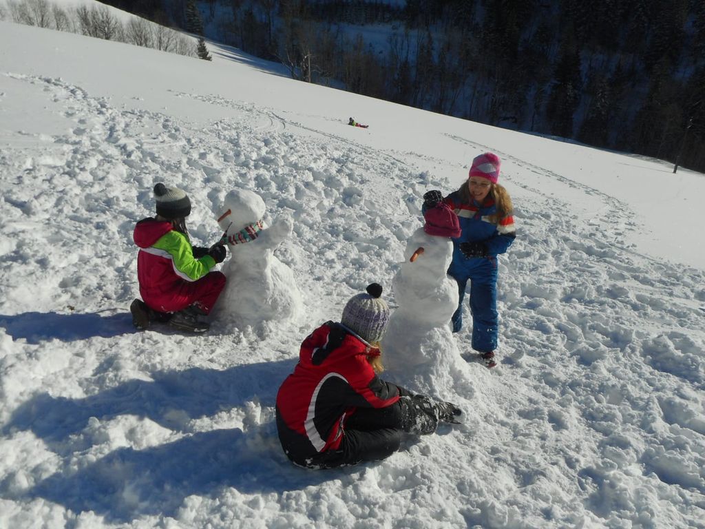 Kinder beim Schneemannbauen im Schnee auf dem Bauernhof.