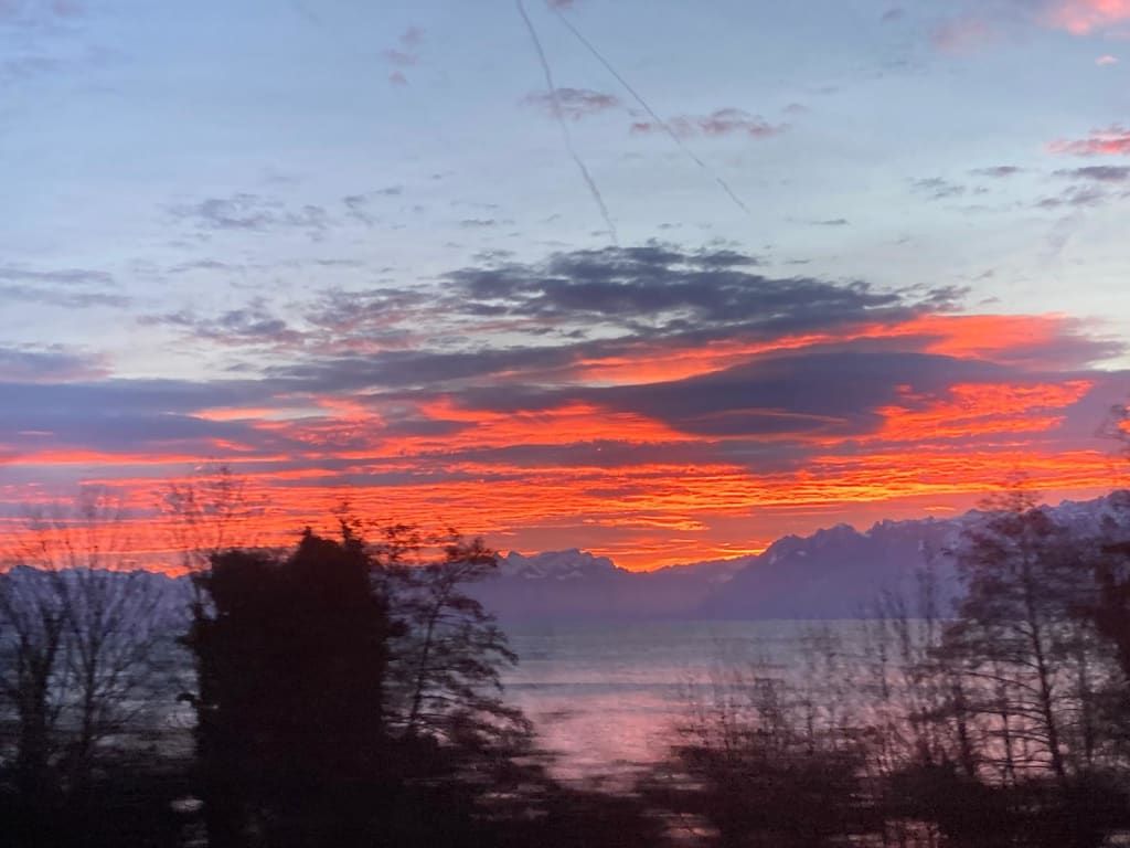 Der rote Abendhimmel über dem See und den schneebedeckten Bergen, sichtbar vom Bauernhof.