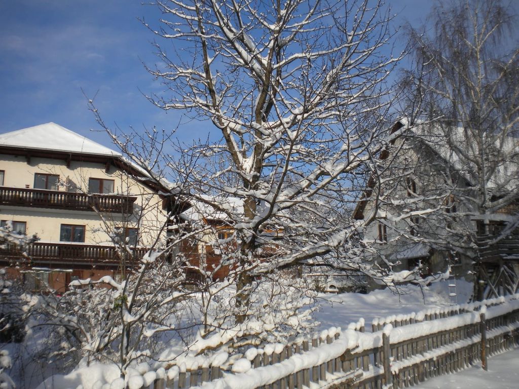Der Bauernhof im Winter, umgeben von Schnee bedeckten Bäumen und einem Holzzaun.