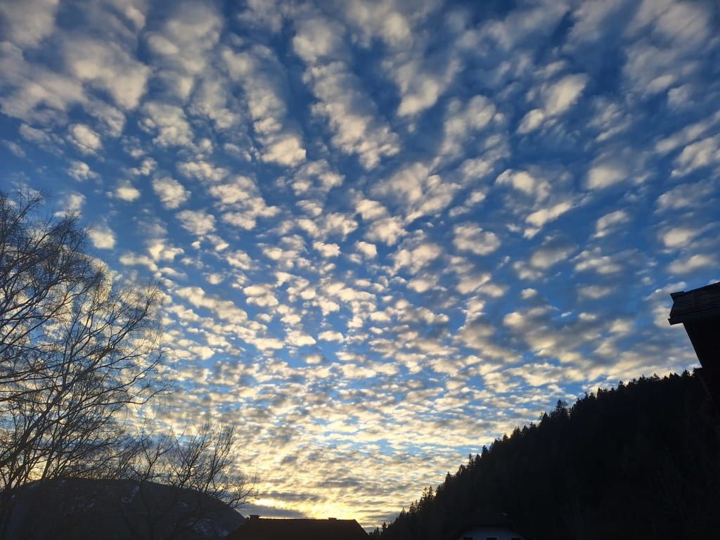 Blick auf den Himmel mit charakteristischen Schäfchenwolken über dem Bauernhof, umgeben von Bäumen und Hügeln.