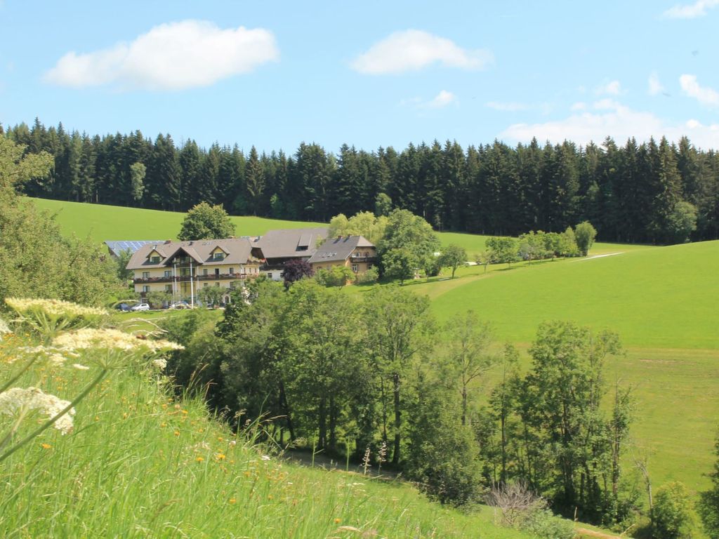 Der Bauernhof liegt eingebettet in eine grüne Landschaft, umgeben von Wiesen und Wäldern.