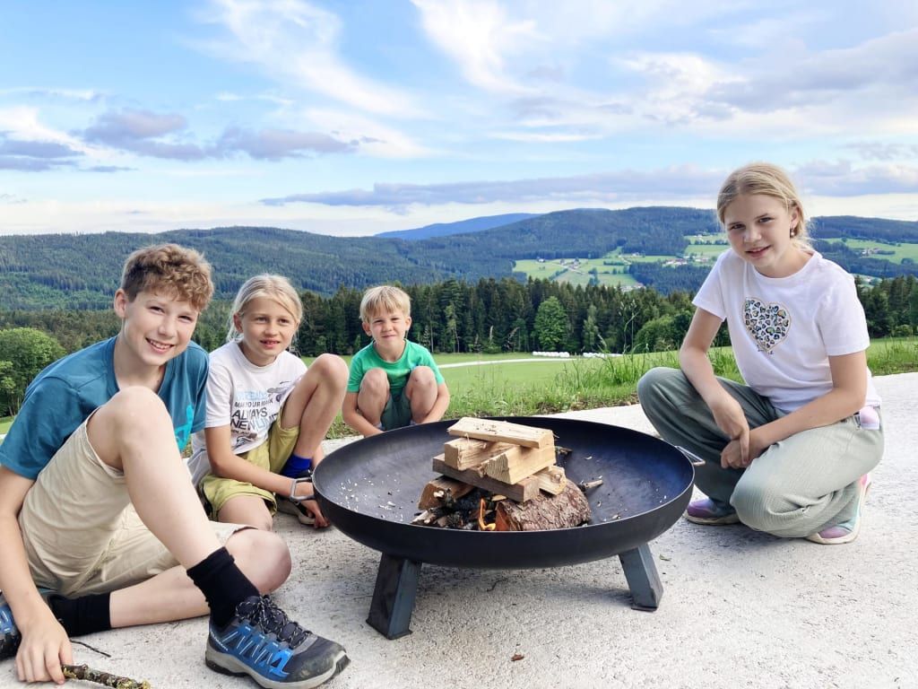 Kinder sitzen um eine Feuerstelle auf dem Bauernhof mit Blick auf die Berge.