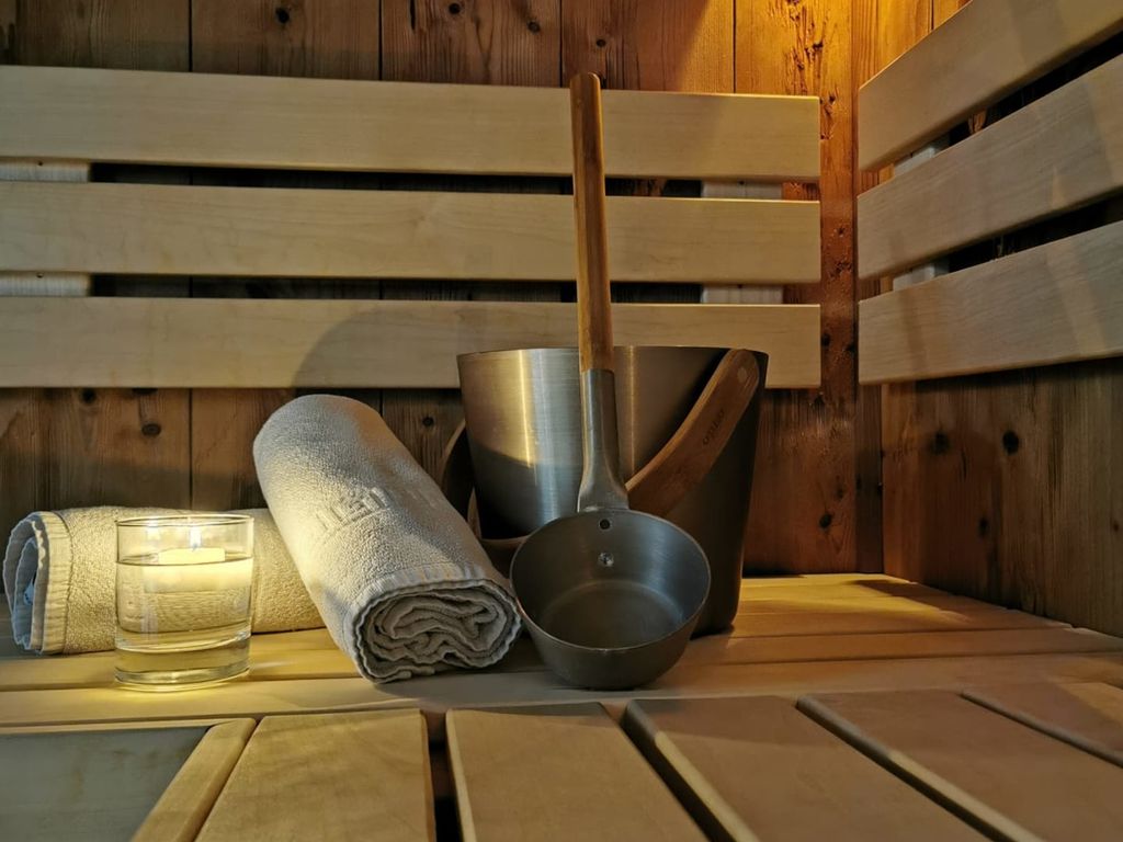 Die Sauna des Bauernhofs mit Holzbänken, Aufgusseimer, Schöpfkelle, Handtüchern und einem Glas Wasser.