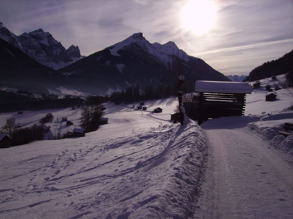 Winterlandschaft um den Bauernhof mit verschneiten Bergen, traditionellen Holzhütten und einem Schneeweg.