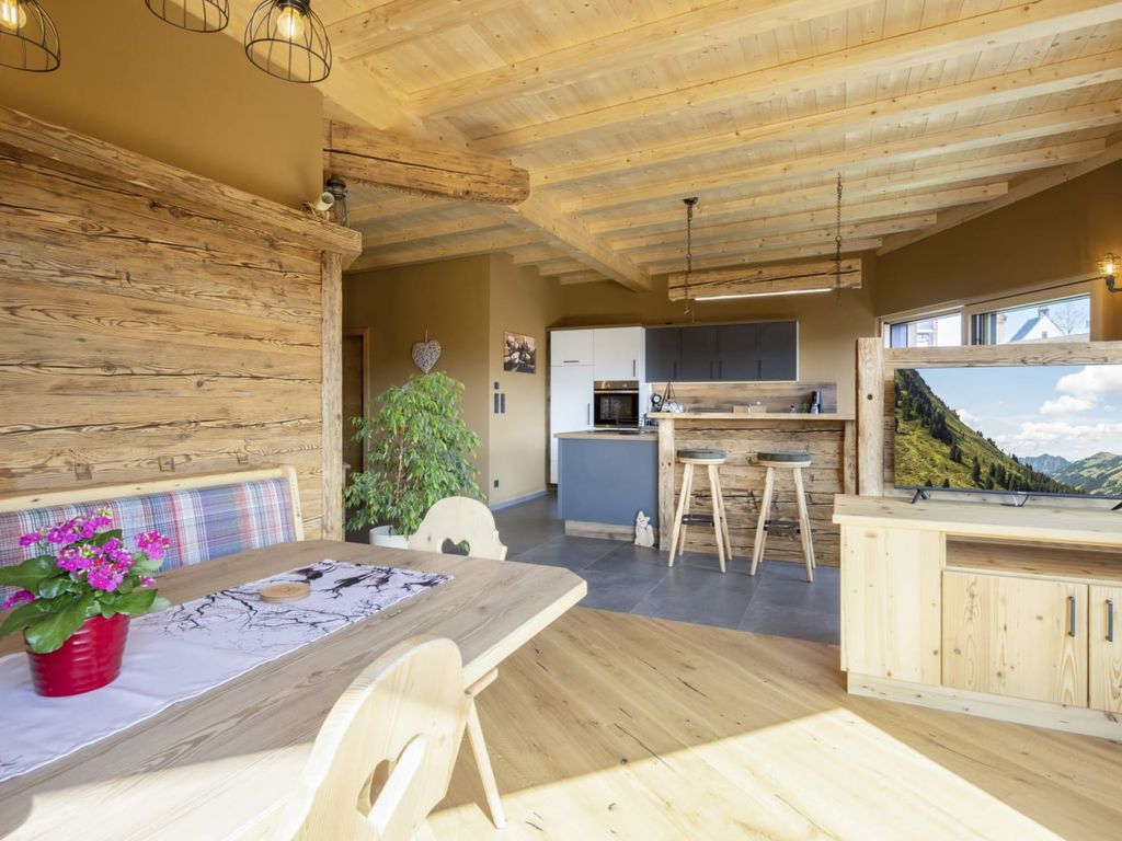 Der offene Wohnbereich des Bauernhofs verfügt über einen Esstisch mit Sitzbank, eine Küche mit Theke und Barhockern sowie einen Fernseher auf einem Holzmöbel.