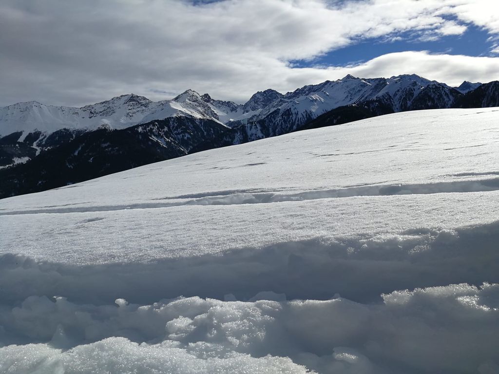 Schneebedeckte Berglandschaft rund um den Bauernhof mit Skispuren im Vordergrund.