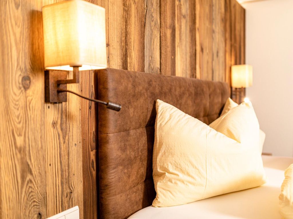 Schlafzimmer im Bauernhof mit gepolstertem Kopfteil, Holzwandverkleidung und Wandleuchte mit integriertem Leselicht.