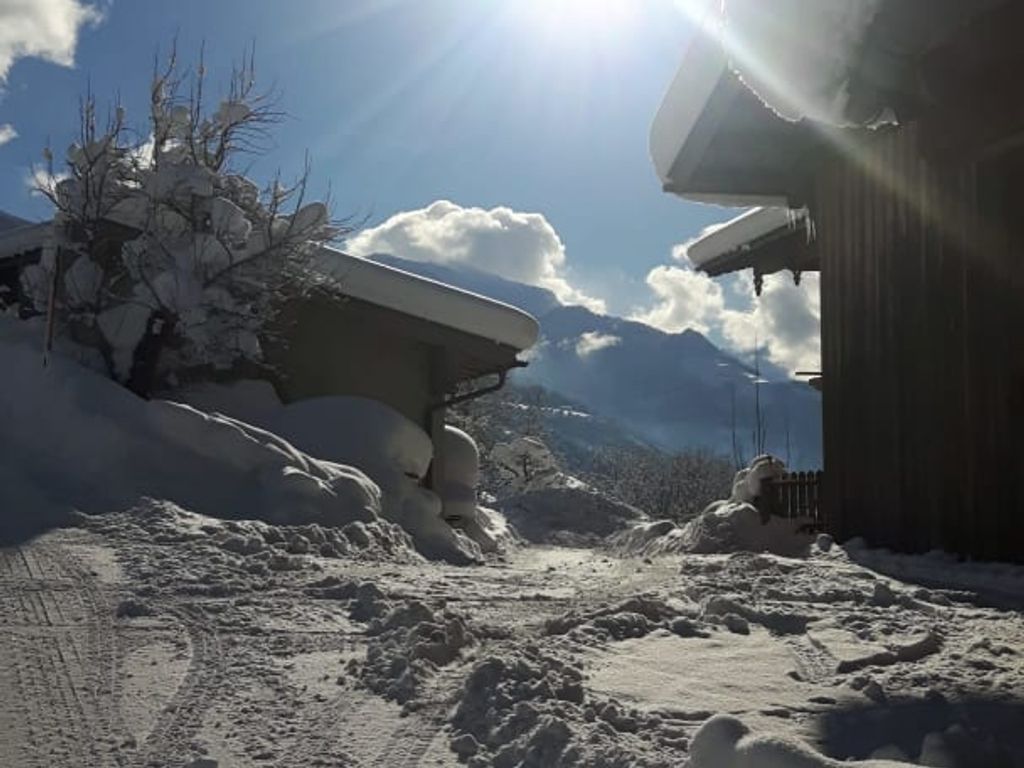 Sonnige Winterlandschaft am Bauernhof mit verschneiten Wegen und Bergblick.