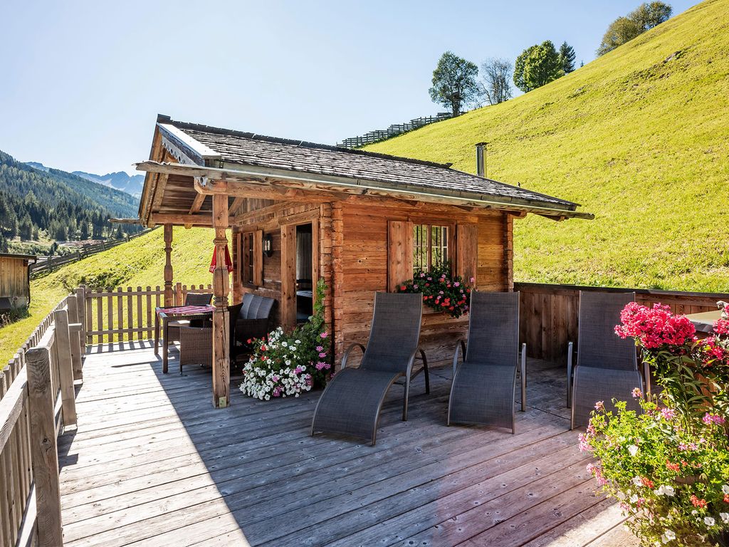 Die Holzhütte auf dem Bauernhof mit Holzterrasse, ausgestattet mit Liegestühlen und Sitzgelegenheiten, bietet einen Ausblick auf die grüne Hügellandschaft.