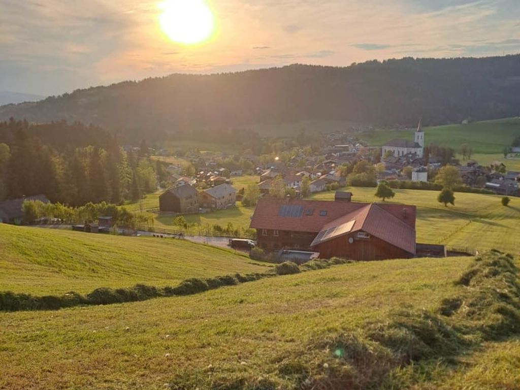 Blick über die grünen Felder auf den Bauernhof und das Dorf im Tal bei Sonnenuntergang.
