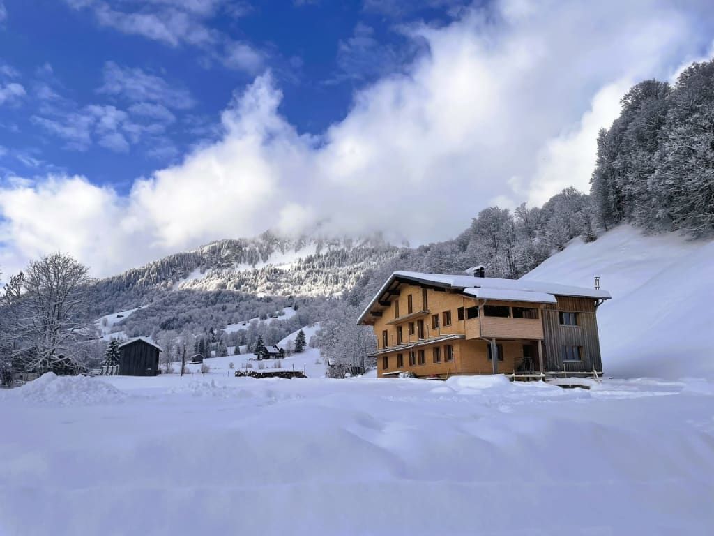 Das Wohnhaus mit Holzfassade und Balkonen, eingebettet in eine verschneite Berglandschaft.
