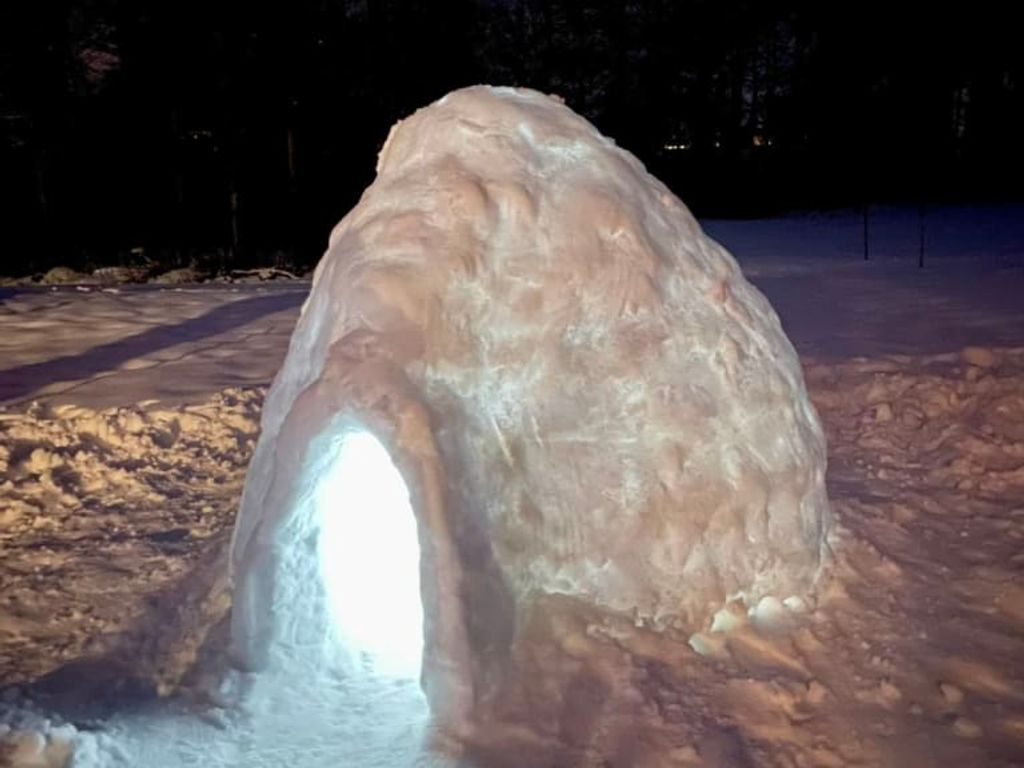Ein stimmungsvoll beleuchtetes Iglu im verschneiten Außenbereich der Ferienwohnung bei Nacht.