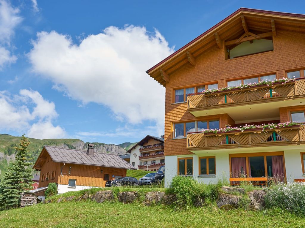Außenansicht des Bauernhofs mit Holzschindelfassade, blühenden Balkonen und Bergblick.