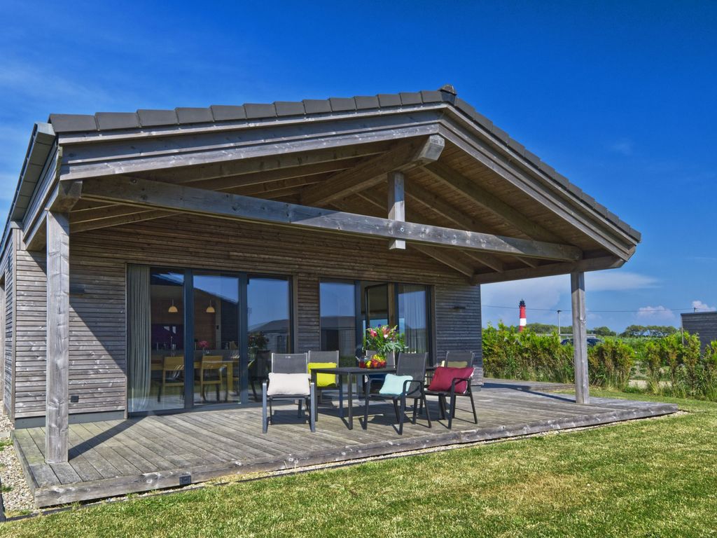 Außenansicht mit überdachter Terrasse und Leuchtturm im Hintergrund